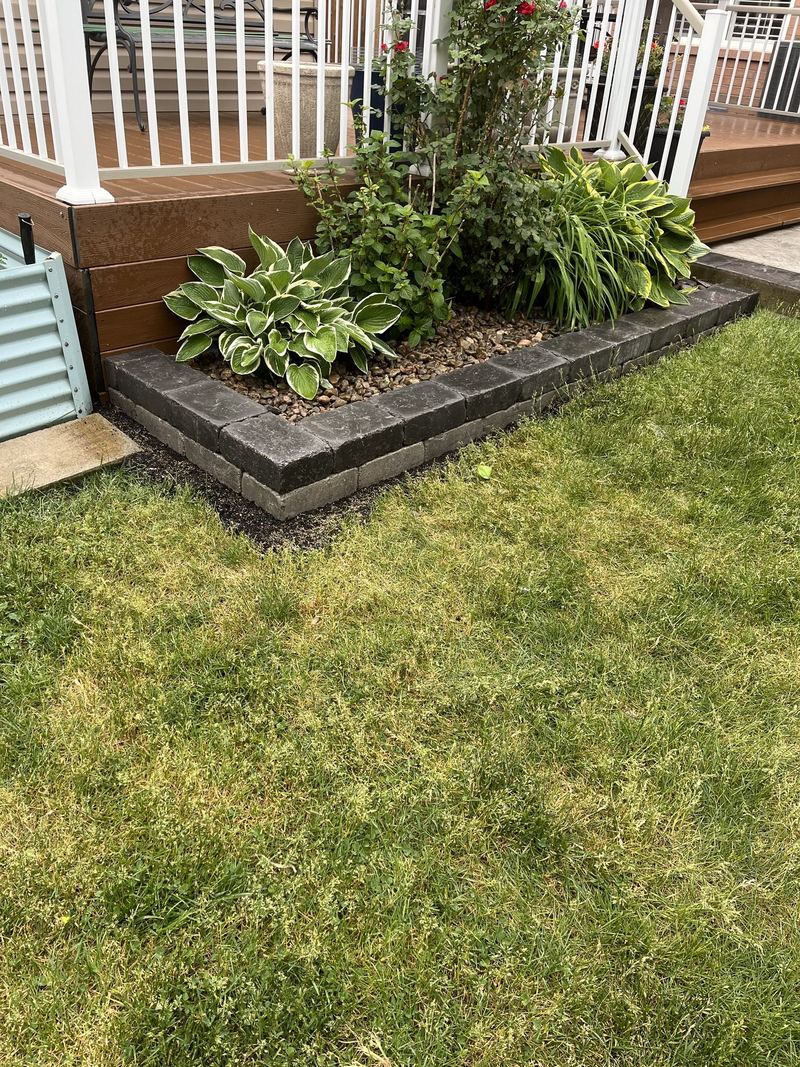Block garden bed edging wrapping a planting bed beside a white deck and hosta plantings