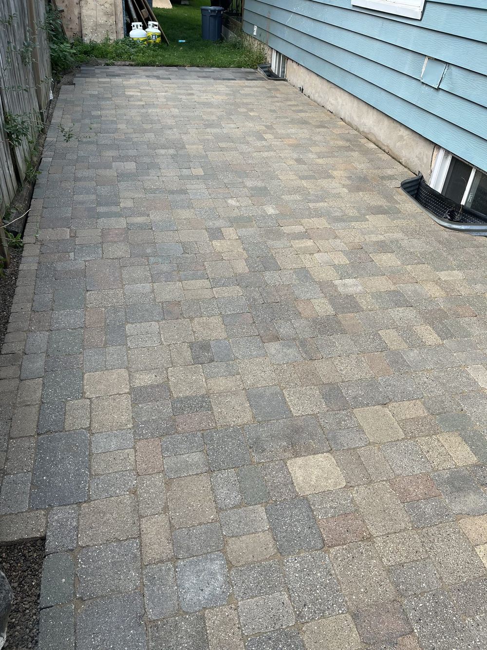 After: the walkway relaid level in cobble pavers, running tight along the house wall with a straight border course