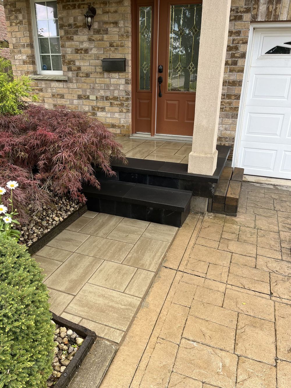 Sandstone slab walkway and front steps leading to a brick house entry, framed by a stone border and planting bed