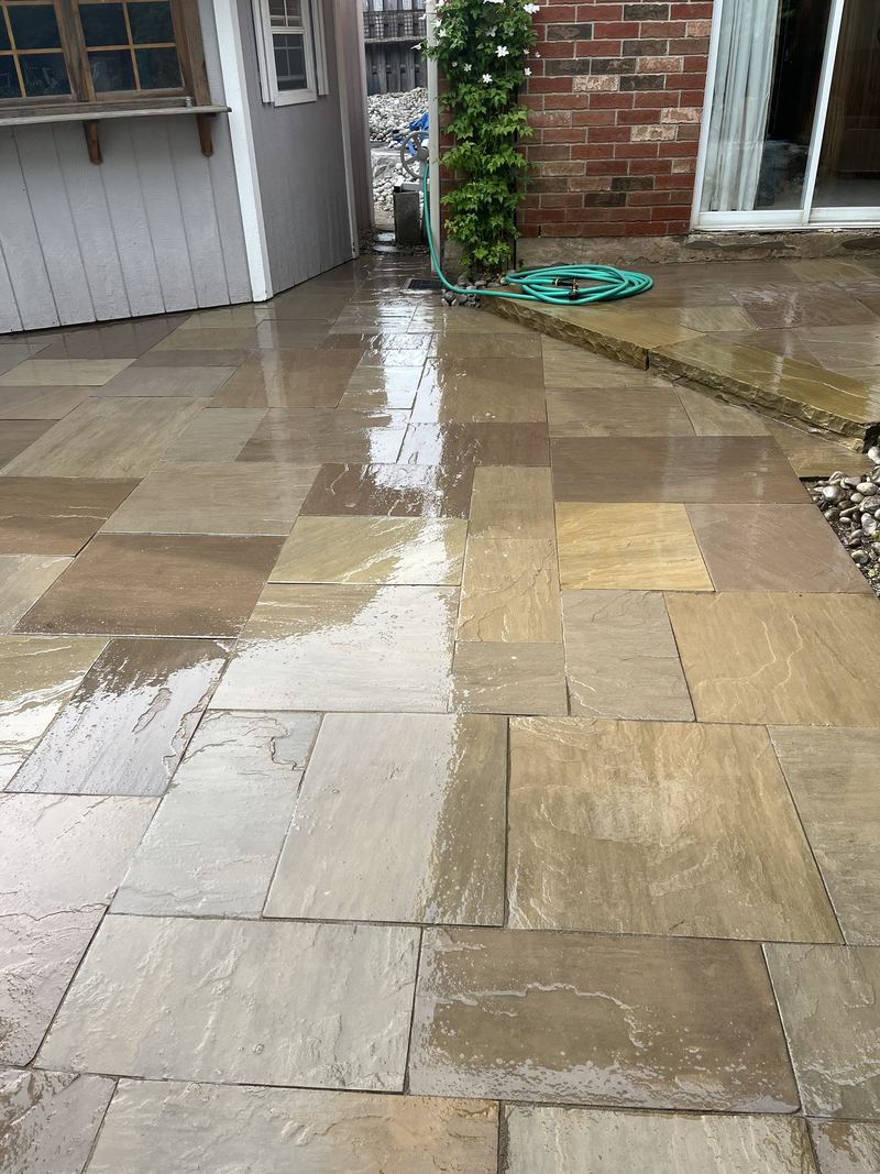 Sandstone slab patio beside a brick and siding house, wet and freshly laid to the back door