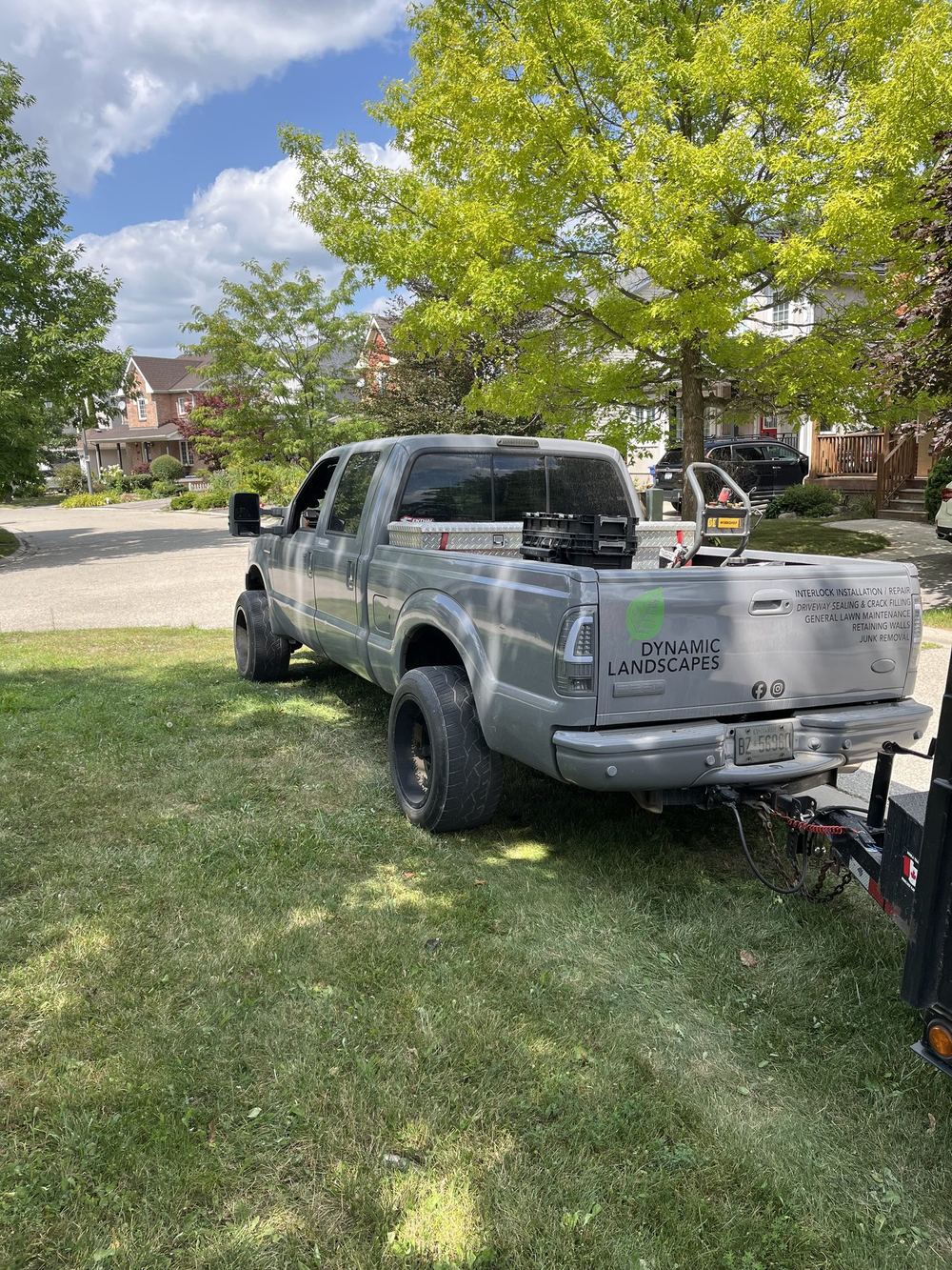 Dynamic Landscapes pickup truck with the company name on the tailgate, parked at a job site with a dump trailer