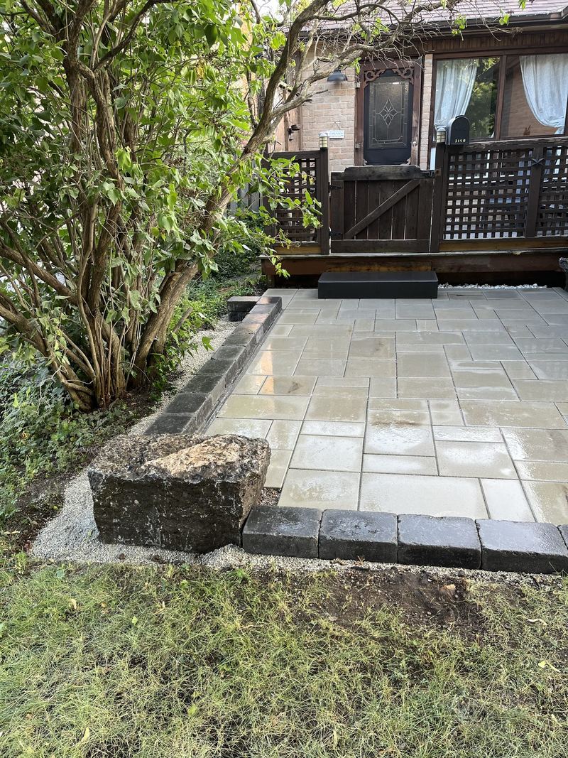 Pale sandstone slab patio beside a deck, framed with a charcoal paver soldier course