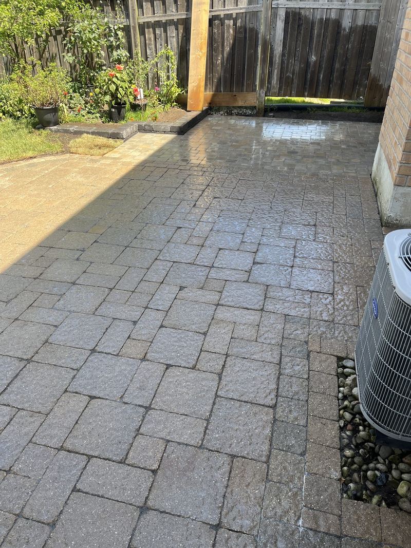 Cobble paver patio running past an air conditioner unit, wet after washing, with a river-rock drainage strip