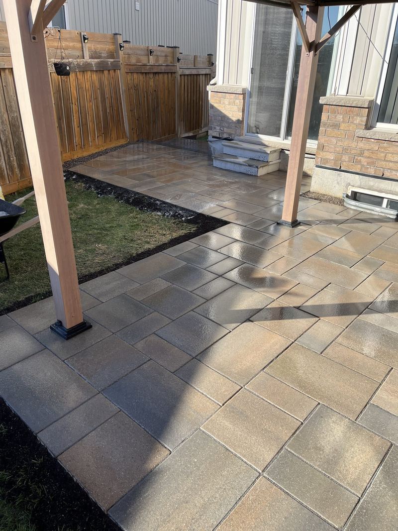 Patio in muted cobble pavers under a timber pergola, with a charcoal border course along the fence